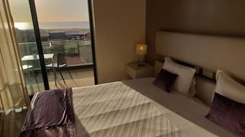 A hotel room with a bed, a nightstand, a lamp, and a view of the ocean through a sliding door.