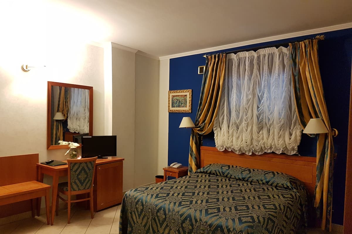 Une chambre d’hôtel comprenant un lit, un bureau avec un ordinateur, une chaise, une lampe et une table de chevet.