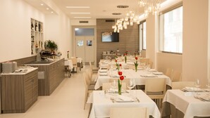 A modern dining area with multiple tables set for service, a kitchen counter, and a television mounted on the wall. - Hotel Ristorante Rinelli (Margherita di Savoia)