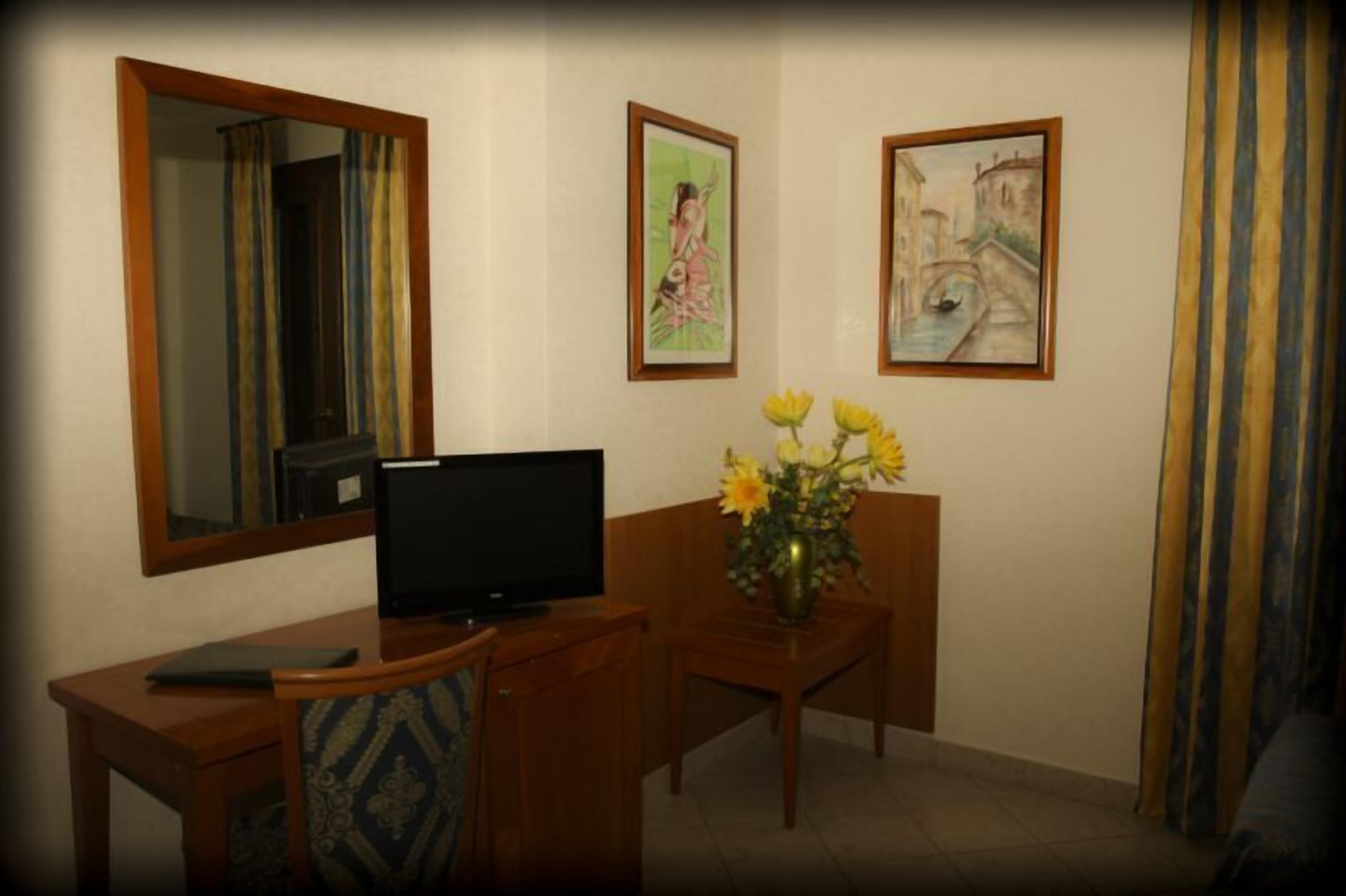 A room with a wooden desk, a television, a vase with flowers, and two framed pictures on the wall.