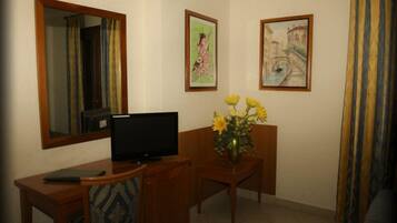 A room with a wooden desk, a television, a vase with flowers, and two framed pictures on the wall.