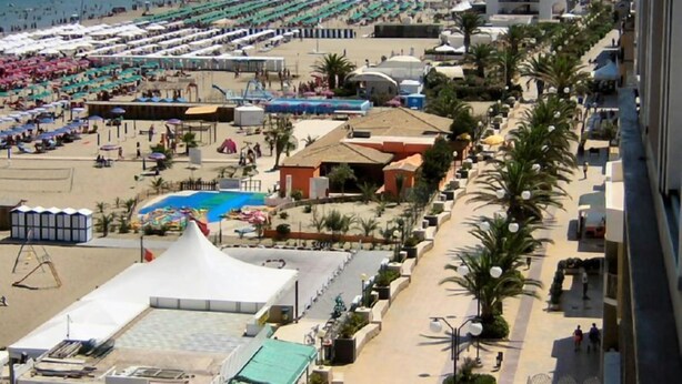A coastal hotel with a beach view, a pool, and a street lined with palm trees. - Hotel Ristorante Rinelli (Margherita di Savoia)