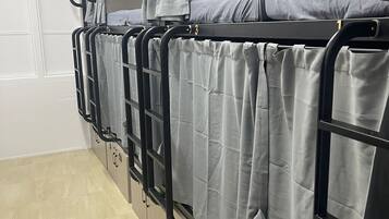 A row of bunk beds with grey bedding, numbered compartments, and a tiled floor.