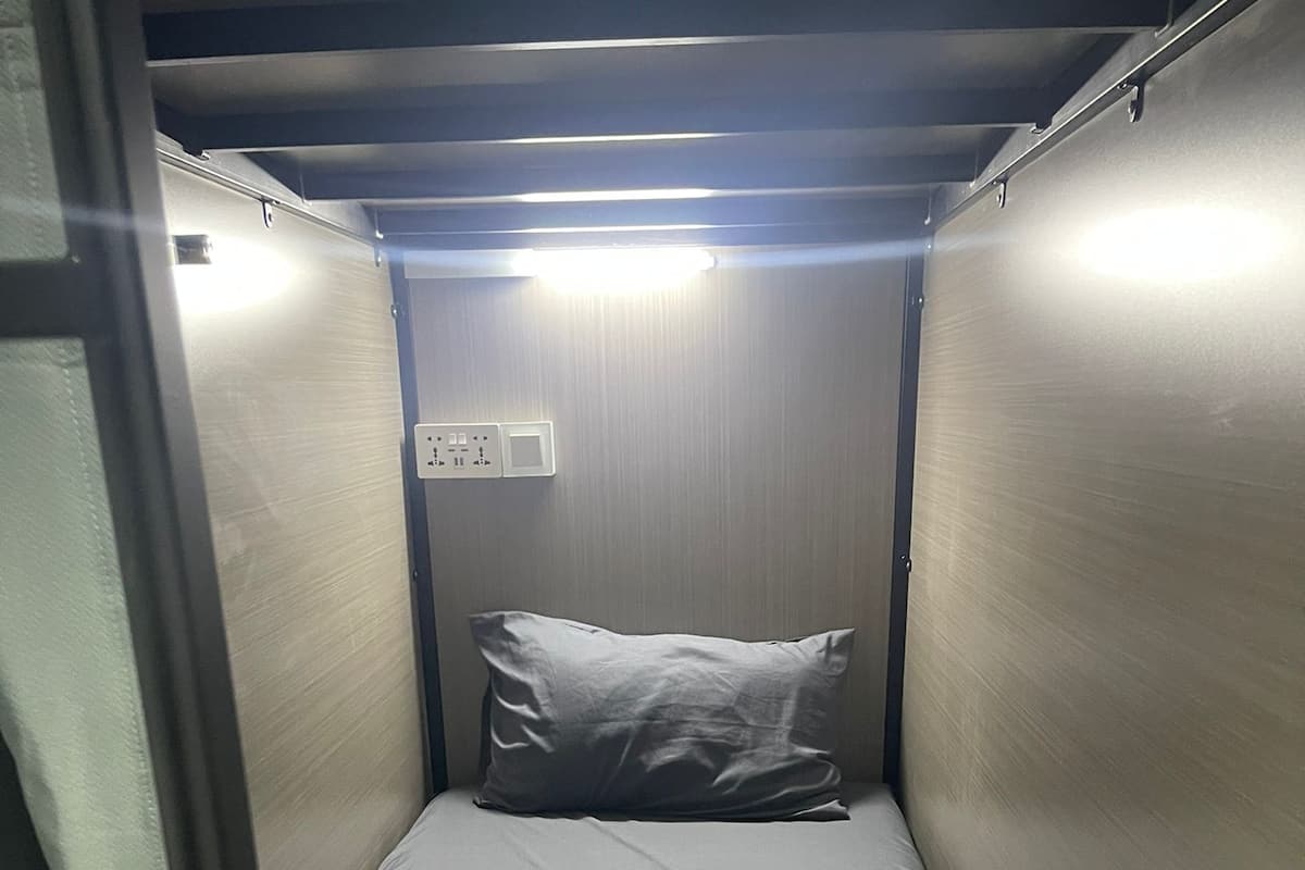 A small, narrow room with a single bed, a pillow, and a blanket.