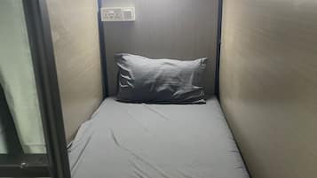 A small, narrow room with a single bed, a pillow, and a blanket.