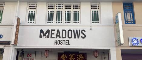 A hostel named "MEADOWS HOSTEL" with a red awning and a bicycle parked in front.