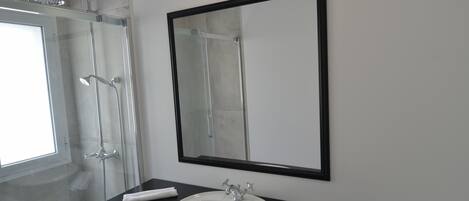 A bathroom with a white sink, a large mirror, and a glass-enclosed shower.
