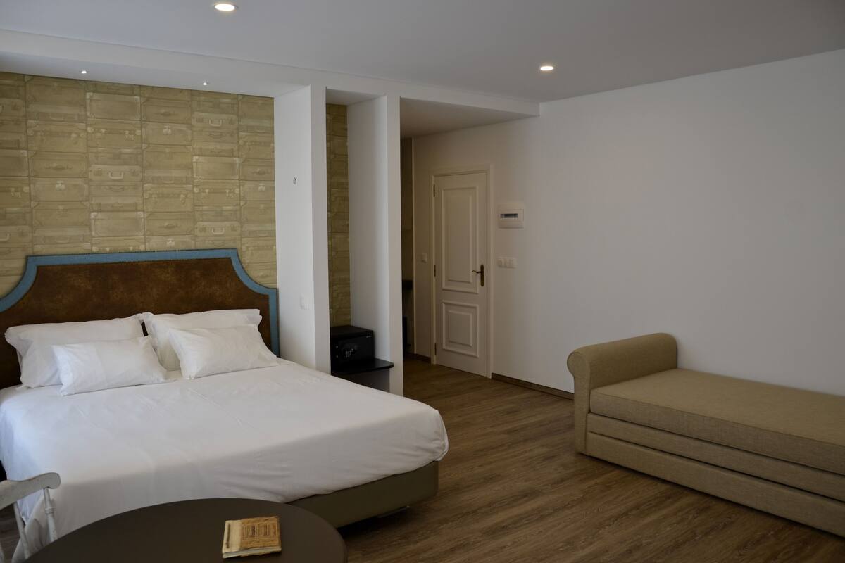 A hotel room with a bed, a sofa, a small table, and a brick-patterned wall.