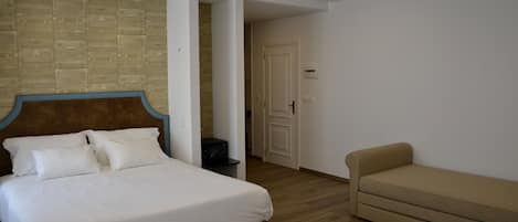 A hotel room with a bed, a sofa, a small table, and a brick-patterned wall.