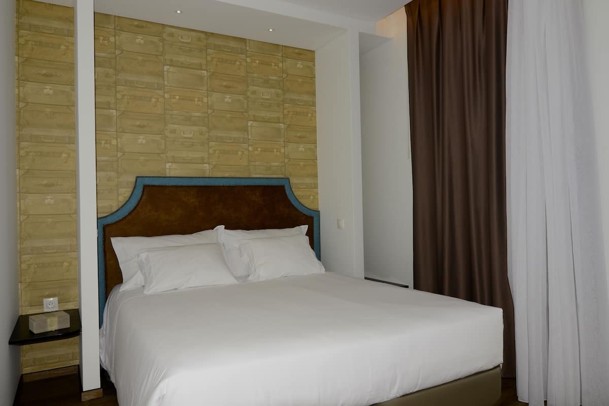 A neatly made bed with white linens in a room with a brick-patterned wall and a wooden headboard.