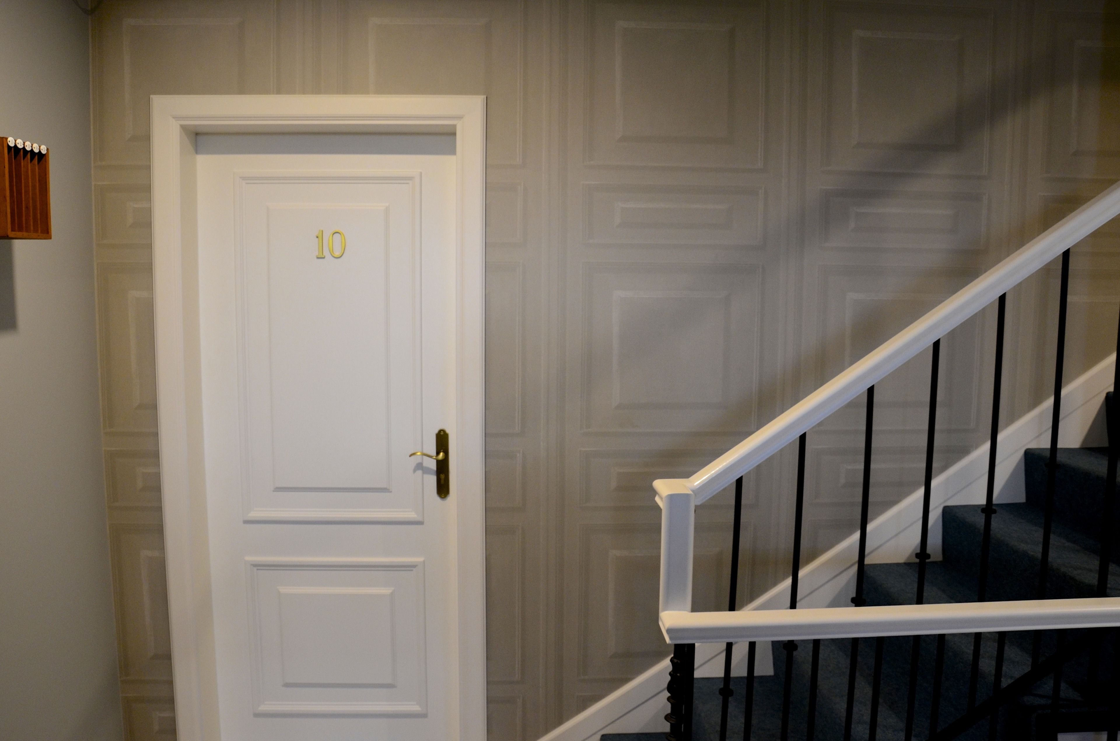 Une porte blanche portant le numéro 10, un escalier avec des rampes noires et un mur orné de motifs.
