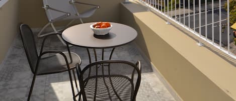 A balcony with a table and chairs, a bowl of fruit, and a view of a cityscape with buildings and a hill.