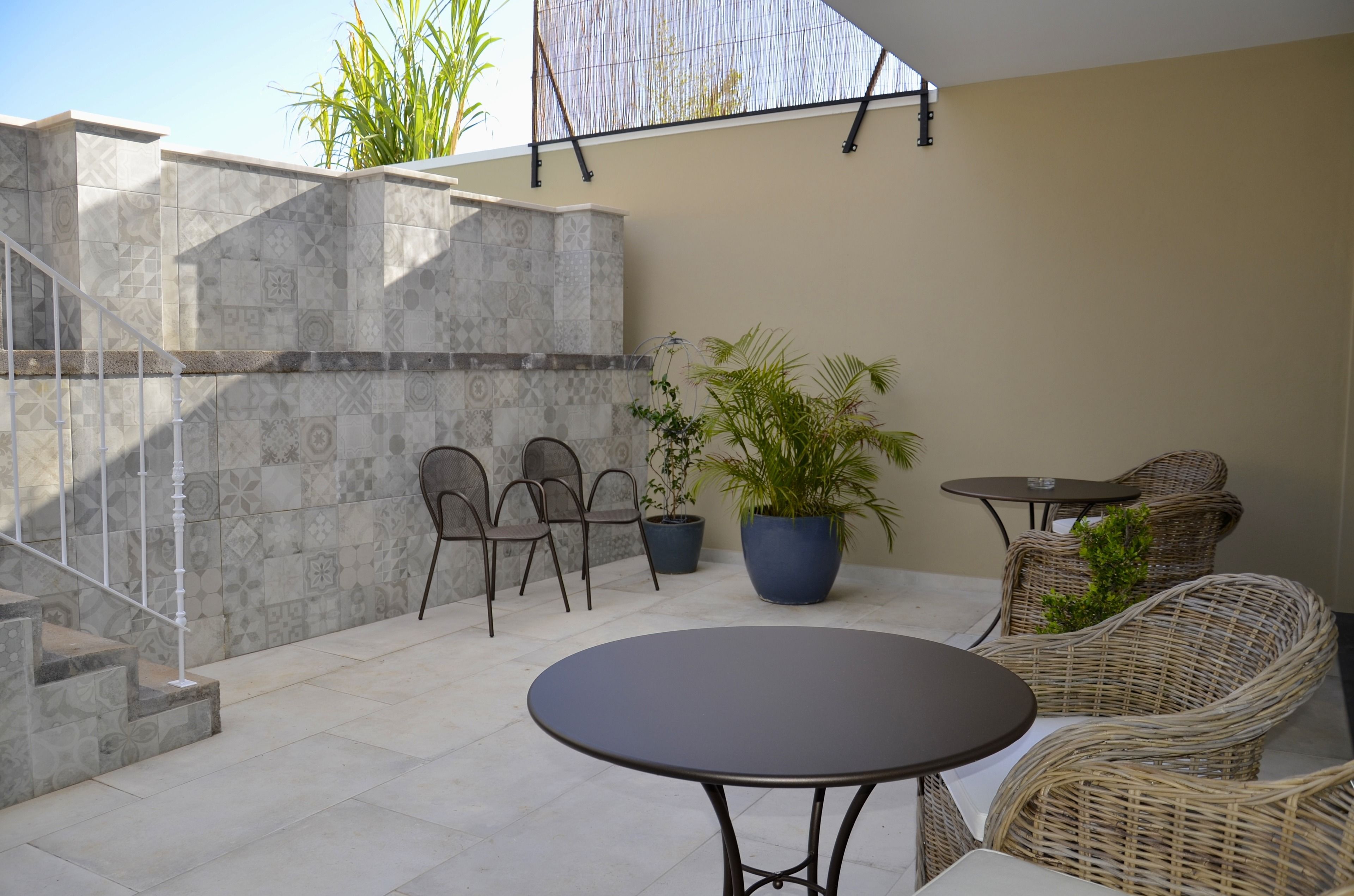A patio area with a round table, wicker chairs, a potted plant, and a staircase.