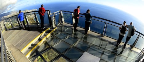 A glass observation deck with a panoramic view of the ocean and distant land.