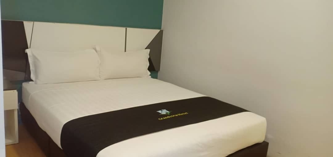 A neatly made bed with a black and white bedspread, a white pillow, and a headboard against a teal wall.