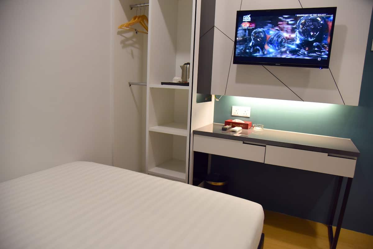 Ein Schlafzimmer mit Bett, Schreibtisch mit Computer, Wand-Fernseher und Kleiderschrank.