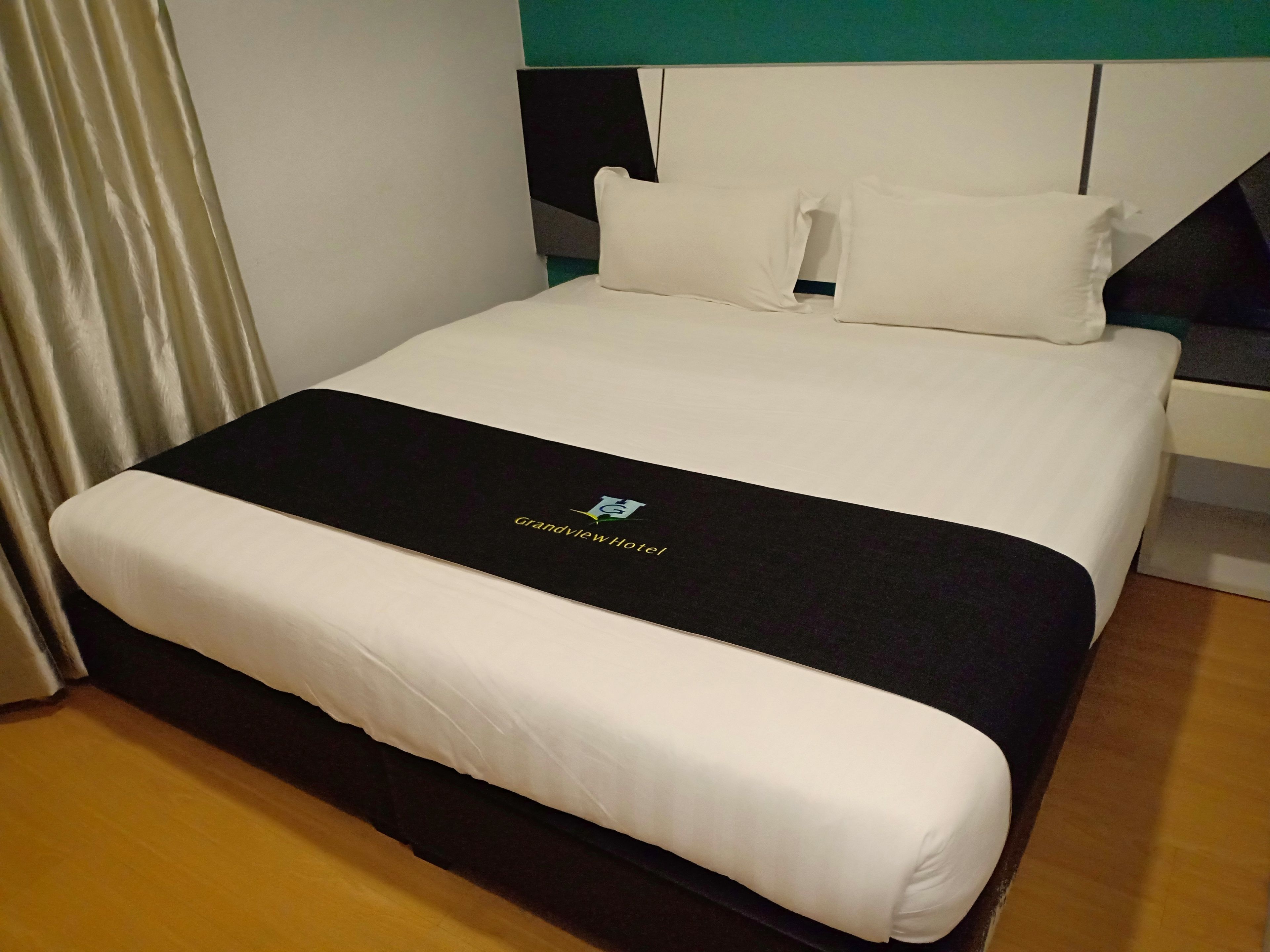 Una habitación de hotel con una cama bien hecha, un cabecero negro y una almohada blanca.