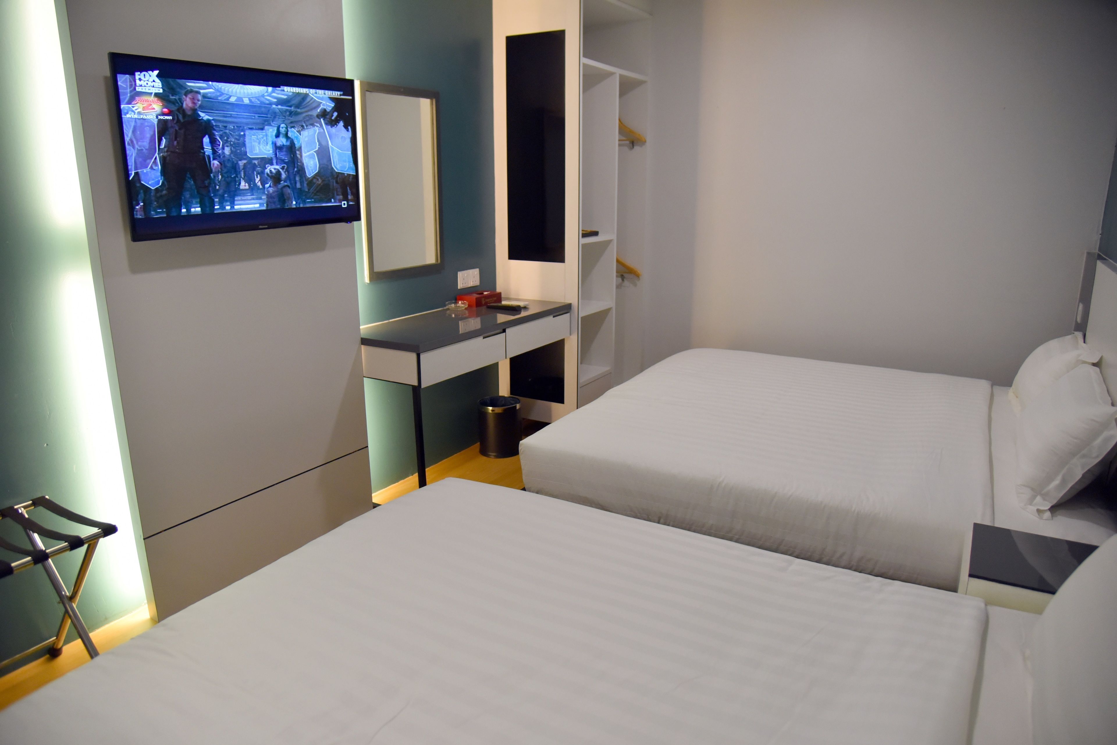Habitación de hotel con dos camas, un televisor montado en la pared, un escritorio y un armario.