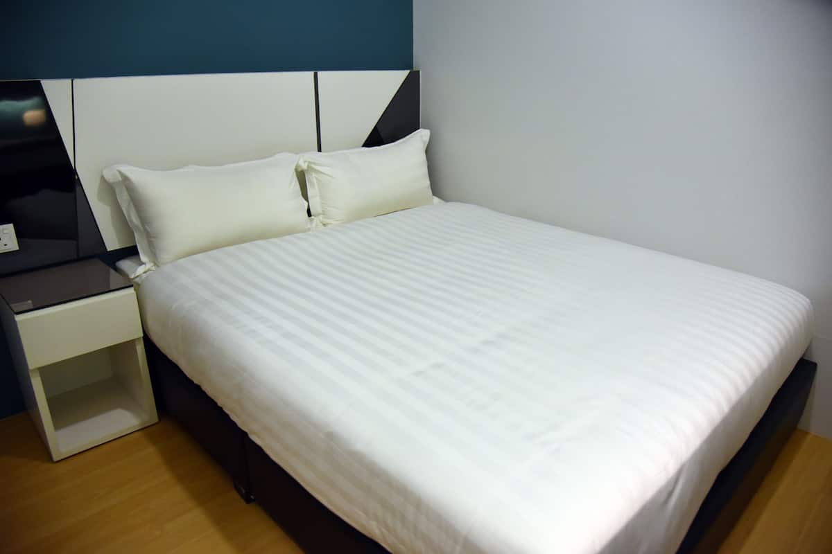 Ein ordentlich bezogenes Bett mit weißer Bettwäsche in einem Zimmer mit modernem Design, inklusive dunkelbraunem Kopfteil und einem weißen Nachttisch.