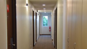 En hotellkorridor med heltäckningsmatta på golvet, dörrar på båda sidor och en brandsläckare på den högra väggen.