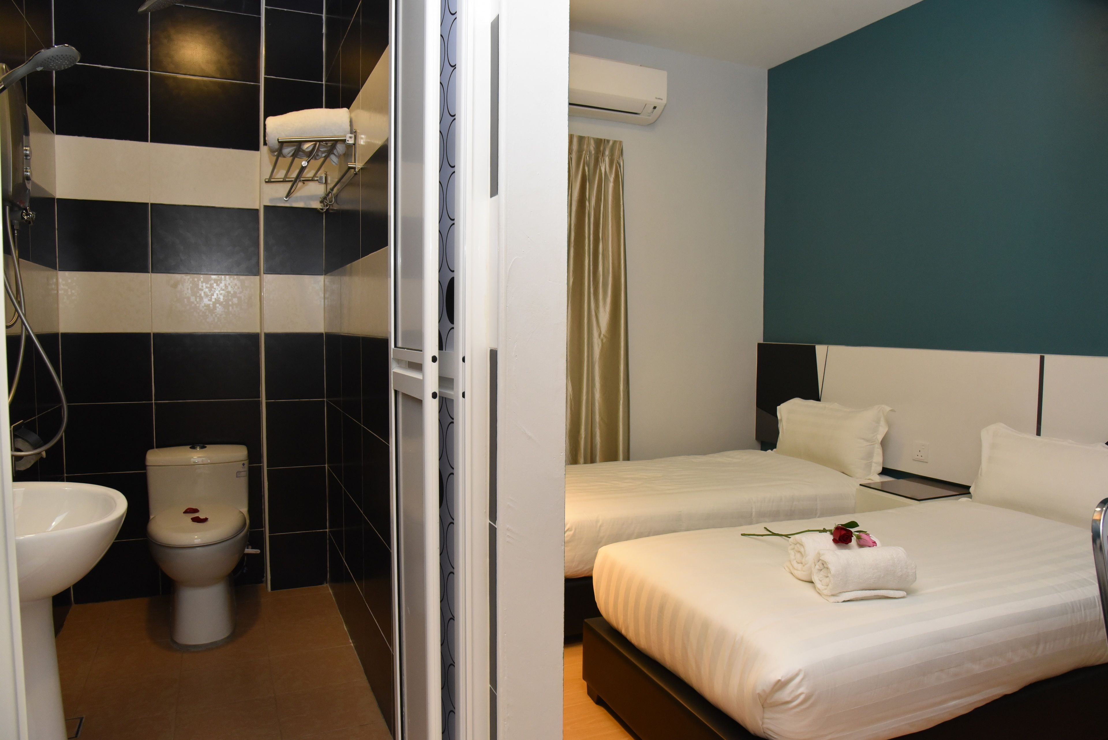 A hotel bathroom with a toilet, sink, and shower. There are two beds with white bedding and a decorative rose on one bed.