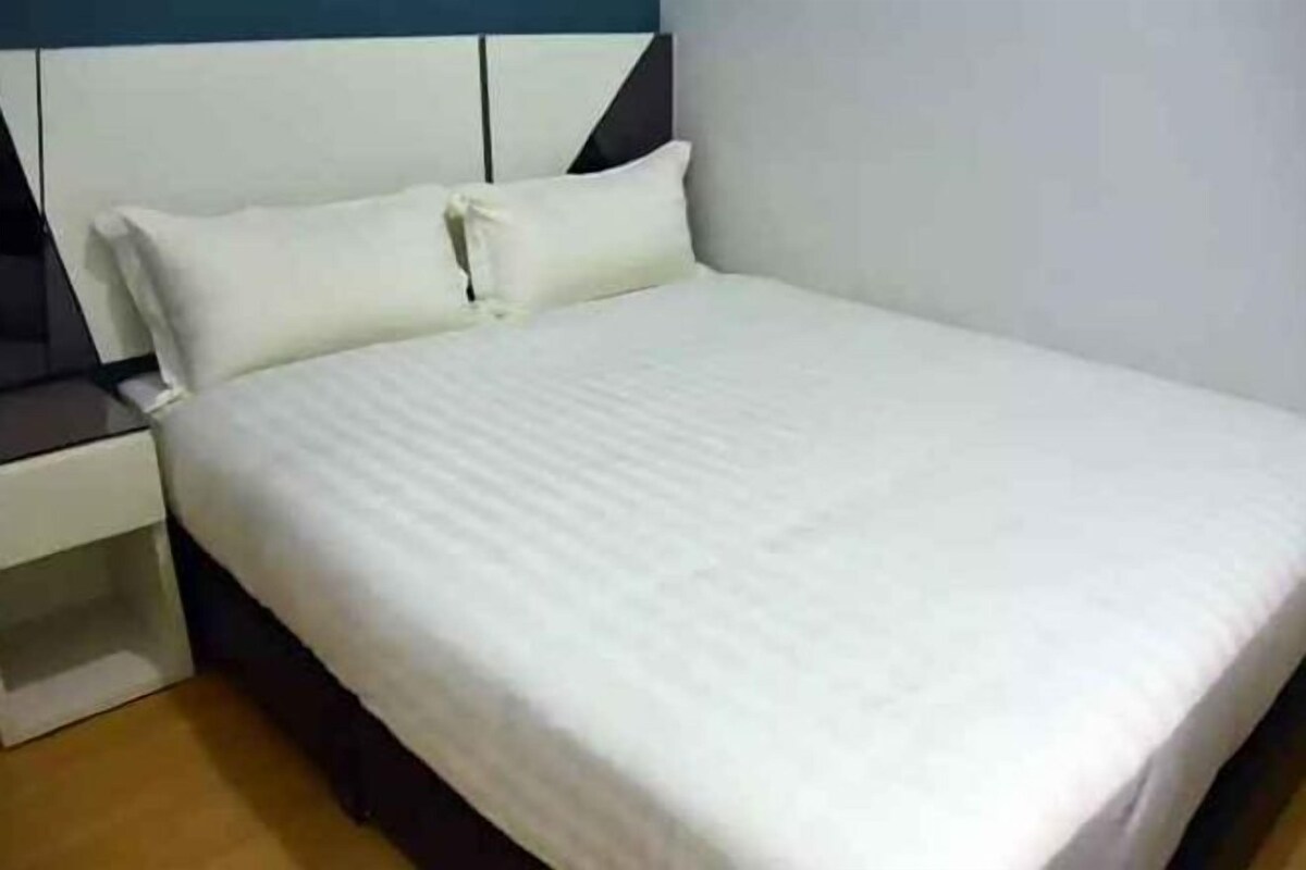 A bed with white bedding, a nightstand with a lamp, and a wooden floor.