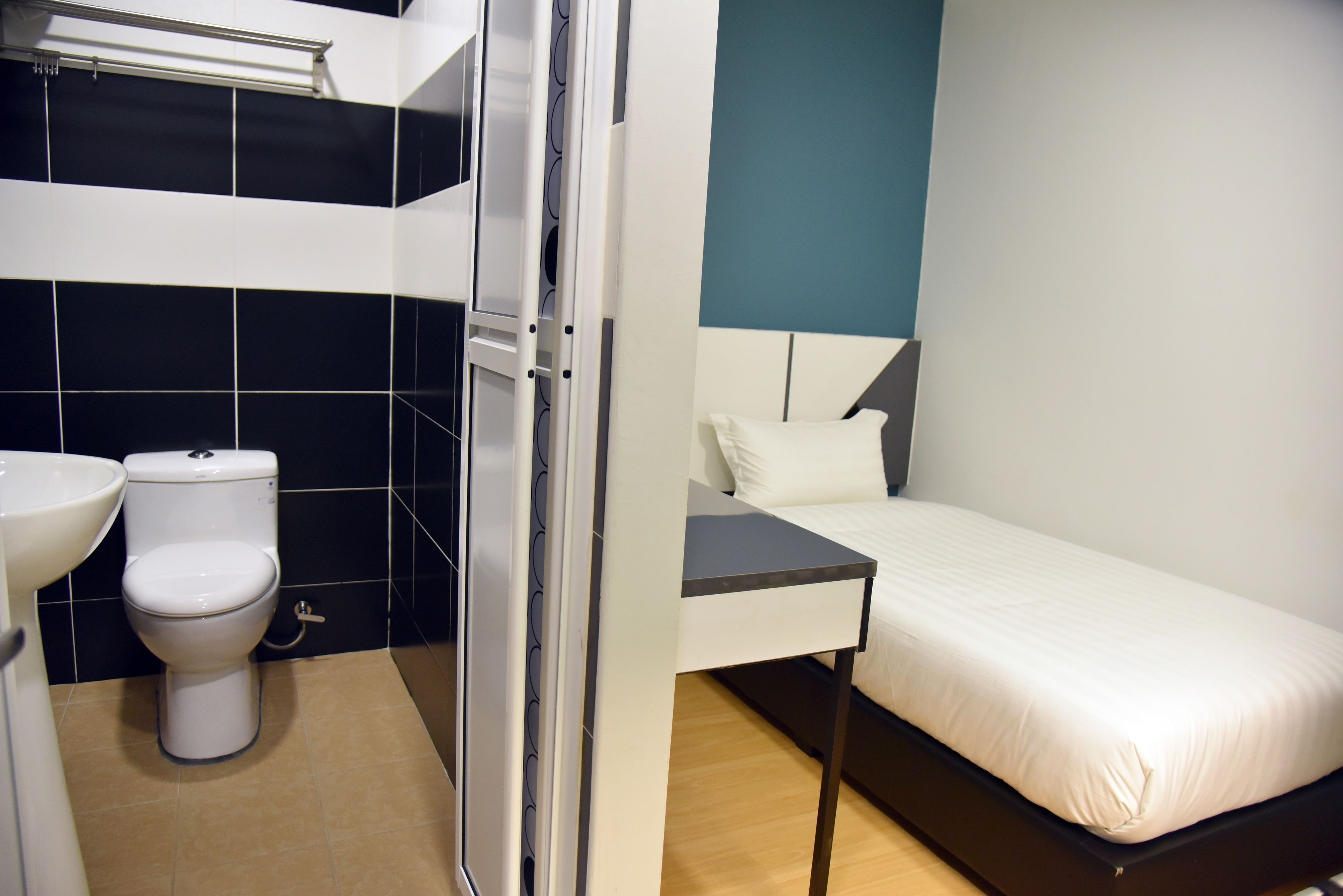 A compact room with a bed, a bedside table, a white toilet, and a sink.