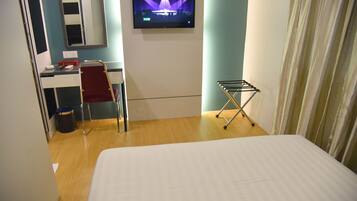 A hotel room with a bed, a desk with a chair, a TV on the wall, and a clothes drying rack.