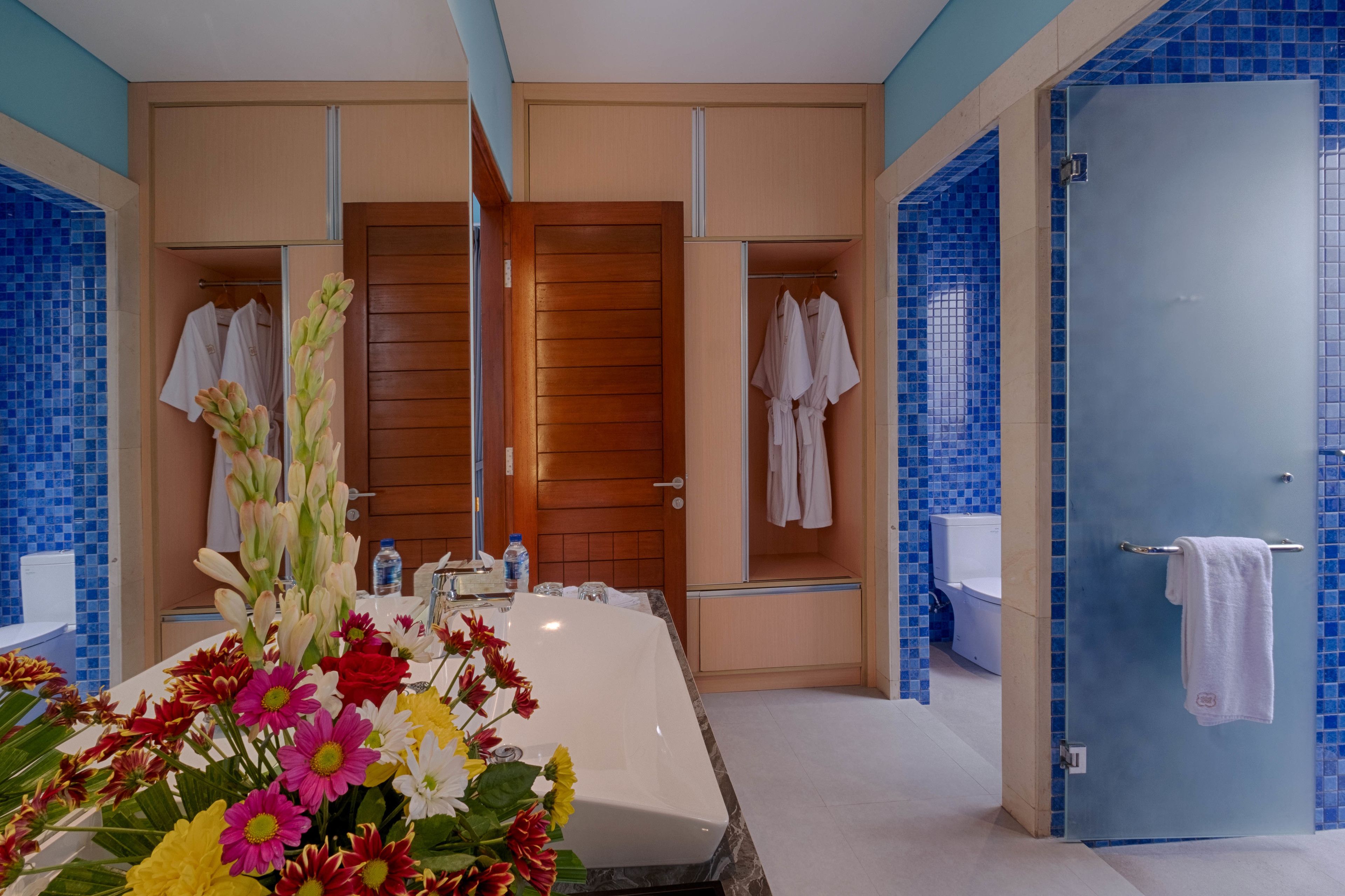 A modern bathroom with a large bathtub, wooden vanity, and blue-tiled walls.