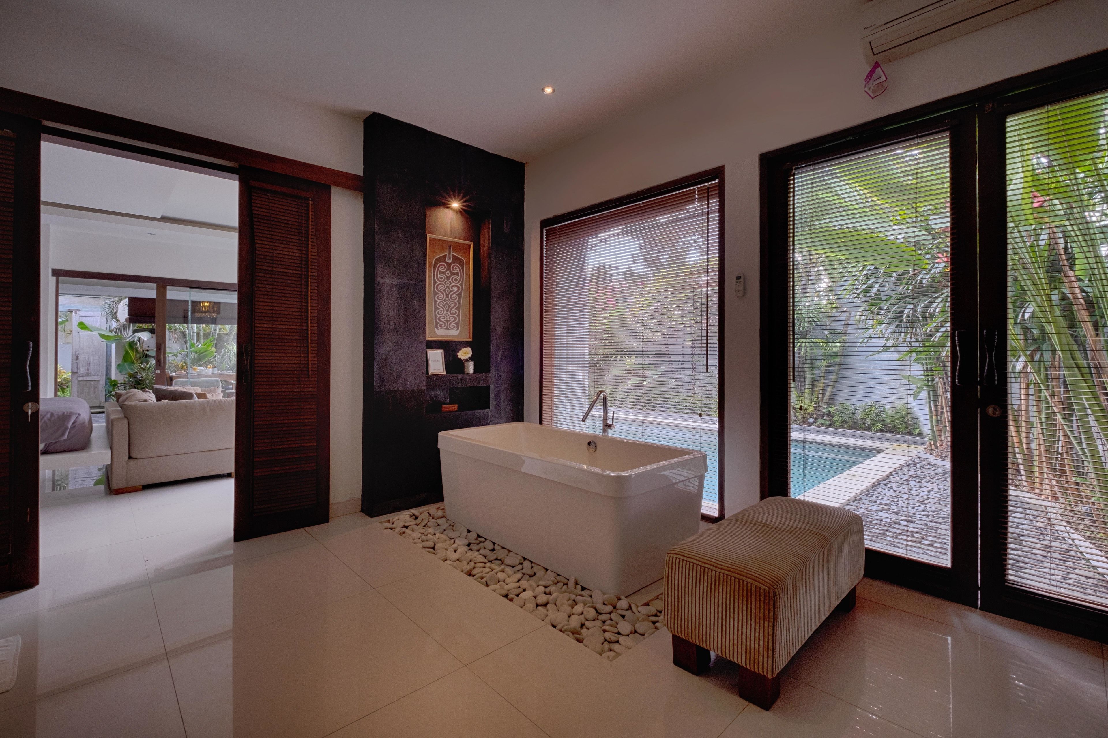 Un bagno moderno con una vasca freestanding, una panca e un'ampia finestra con persiane.