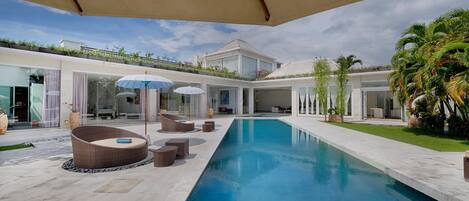 A modern pool area with lounge chairs and umbrellas, surrounded by a well-maintained lawn and a large house in the background.