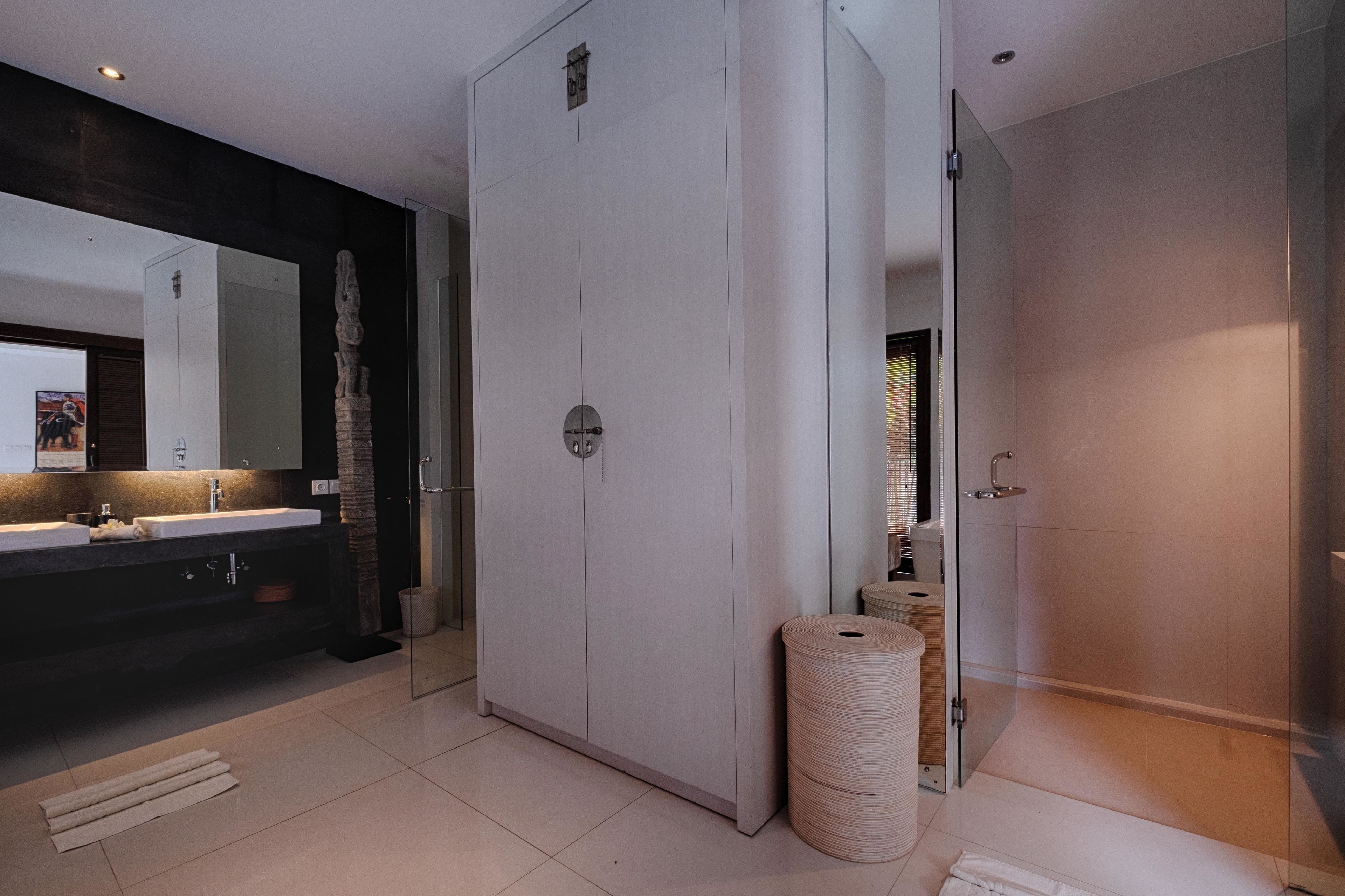 A modern bathroom with a large mirror, a white vanity, a glass shower enclosure, and a towel dispenser.