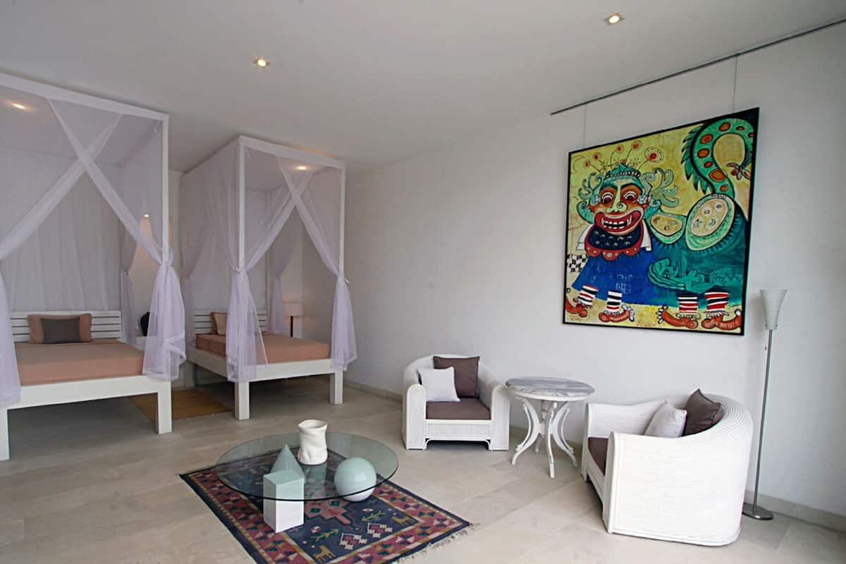 Een slaapkamer met twee bedden, een bank, een kleine tafel en een kleurrijk schilderij aan de muur.