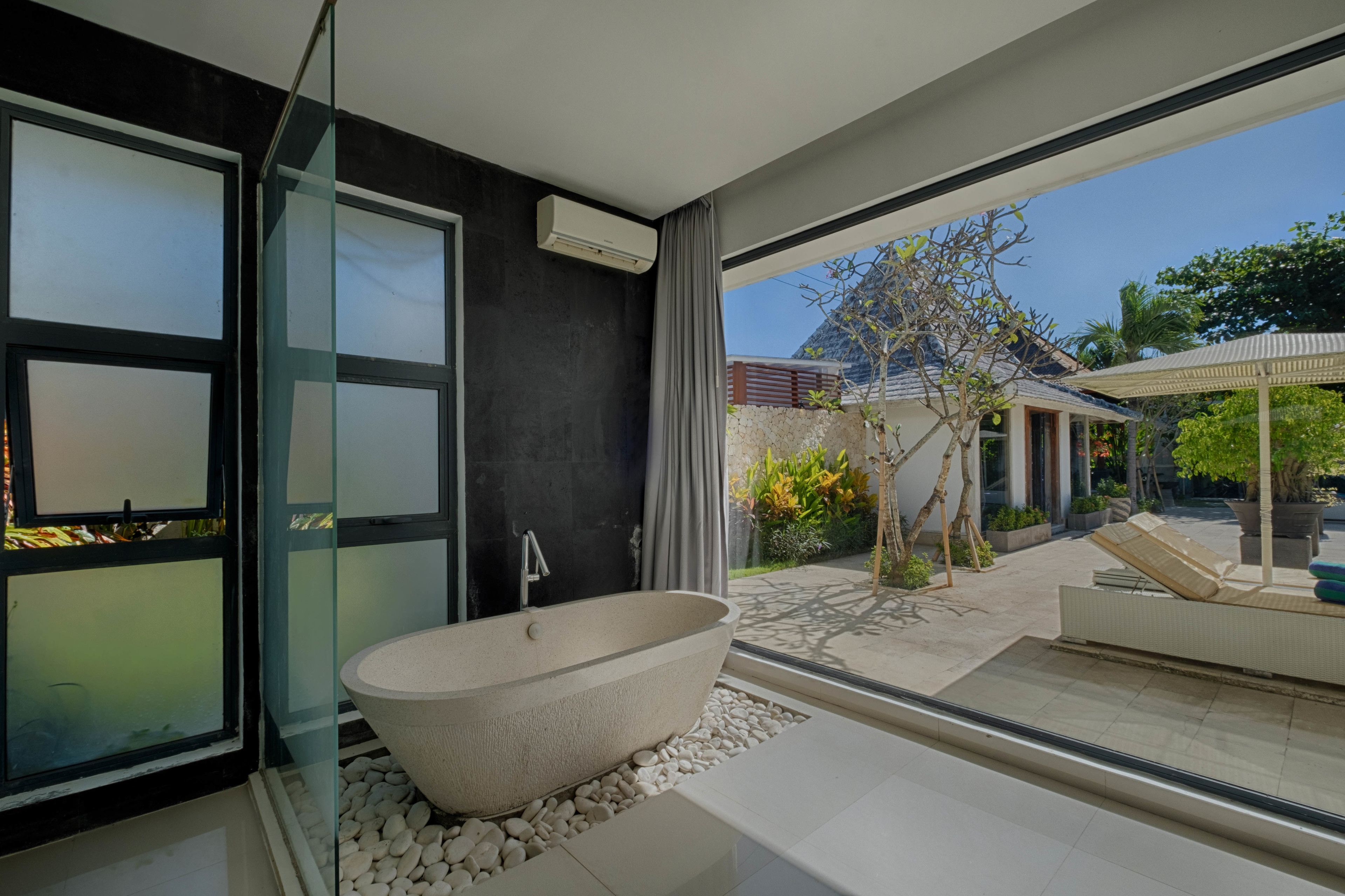 A modern bathroom with a freestanding bathtub, large windows, and a view of the outdoor garden.