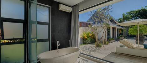 A modern bathroom with a freestanding bathtub, large windows, and a view of the outdoor garden.