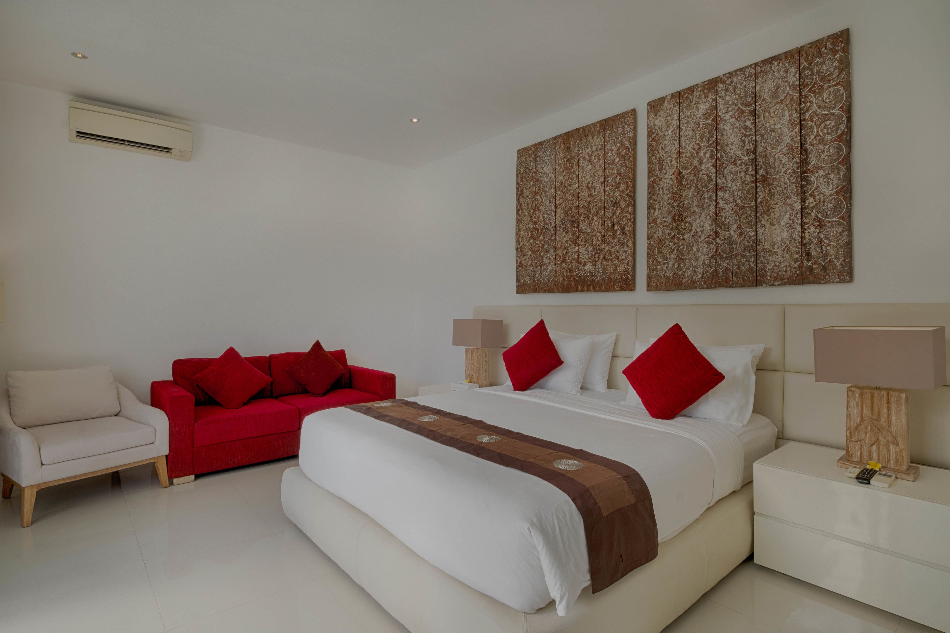 A hotel room with a bed, a red sofa, a nightstand with a lamp, and two large abstract paintings on the wall.