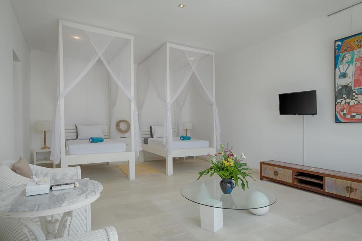 Een moderne kamer met twee witte bedden, een glazen salontafel, een televisie en een kleurrijk schilderij aan de muur.