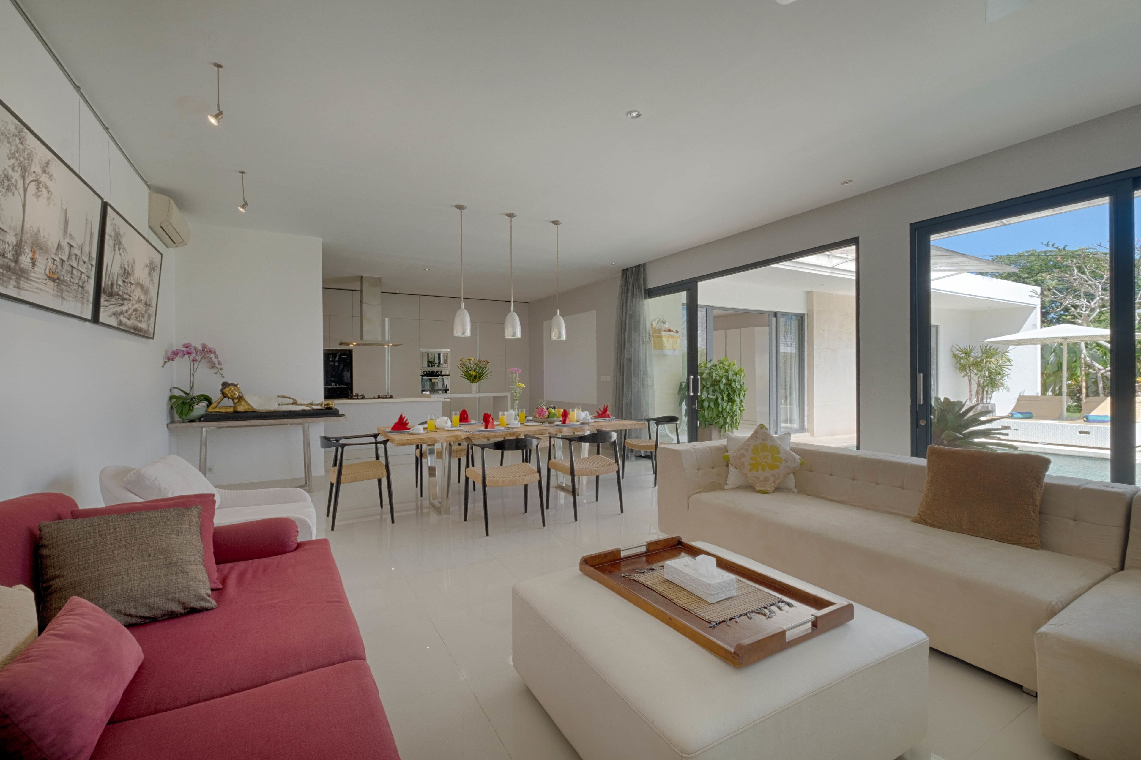 A modern living room with a red sofa, a white sofa, and a dining area with a wooden table and chairs.
