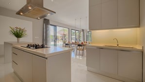 A modern kitchen with a central island, a dining area with a view, and a large window. - Canggu Villa by Sanga Sanga Hospitality (Canggu)