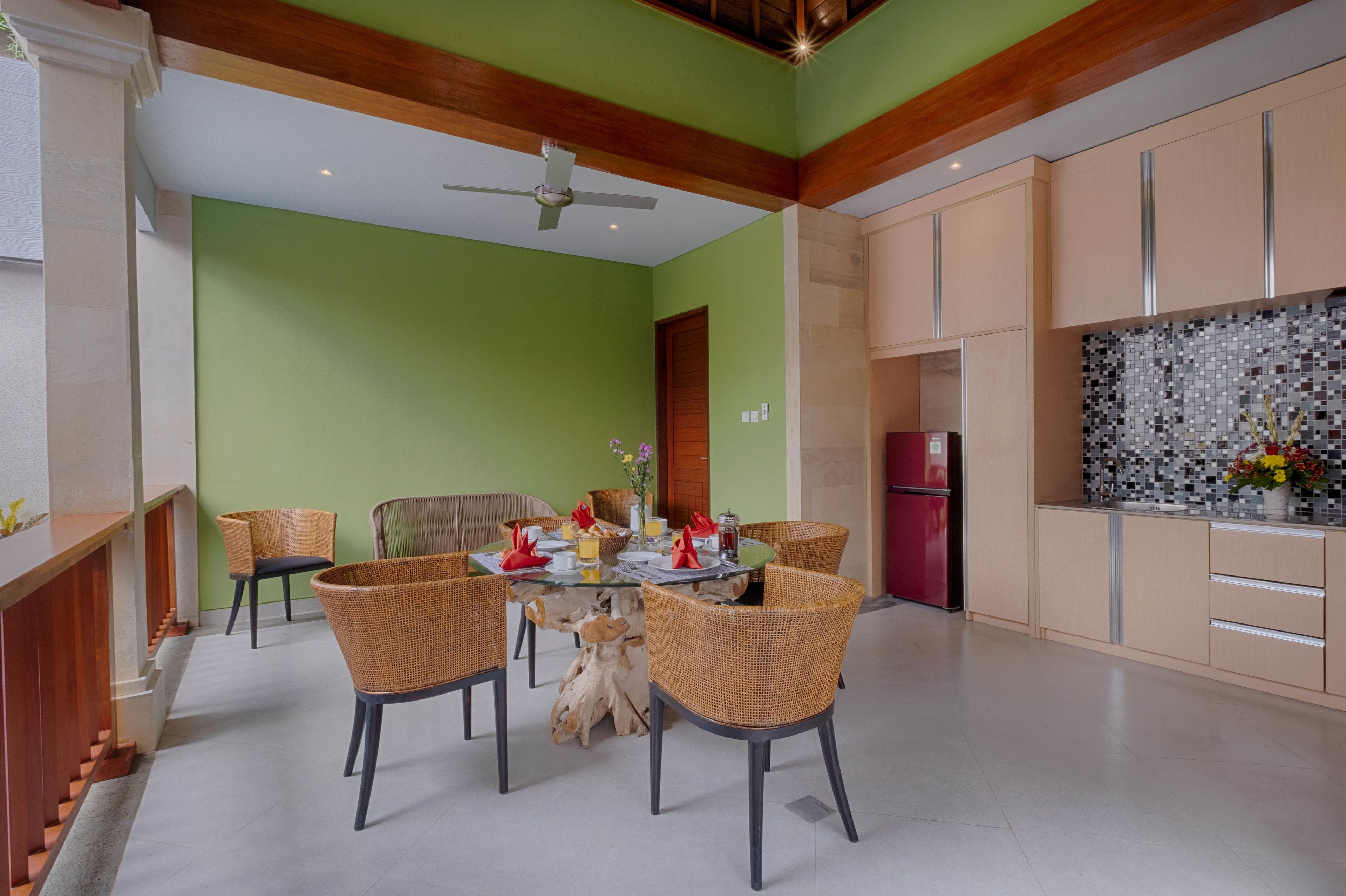 Un coin repas avec une table ronde, des chaises en osier et un ventilateur de plafond.