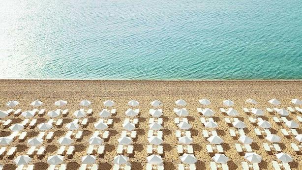A beach with rows of white sun loungers and umbrellas, arranged in a grid pattern. - Hotel Grifid Foresta  Adults Only (Golden Sands)