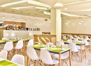 A modern dining area with multiple tables and chairs, a central bar area, and pendant lighting. - Hotel Grifid Foresta  Adults Only (Golden Sands)
