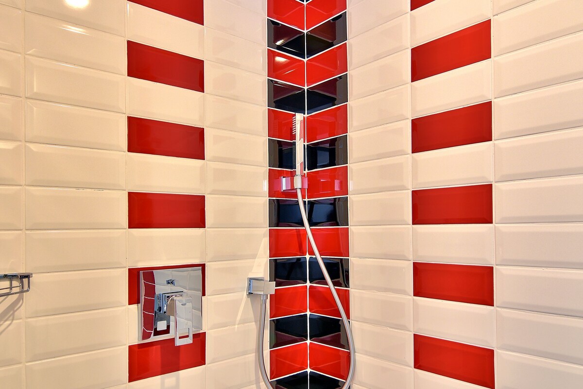 A bathroom with red and white striped walls, a shower, and a ceiling light fixture.