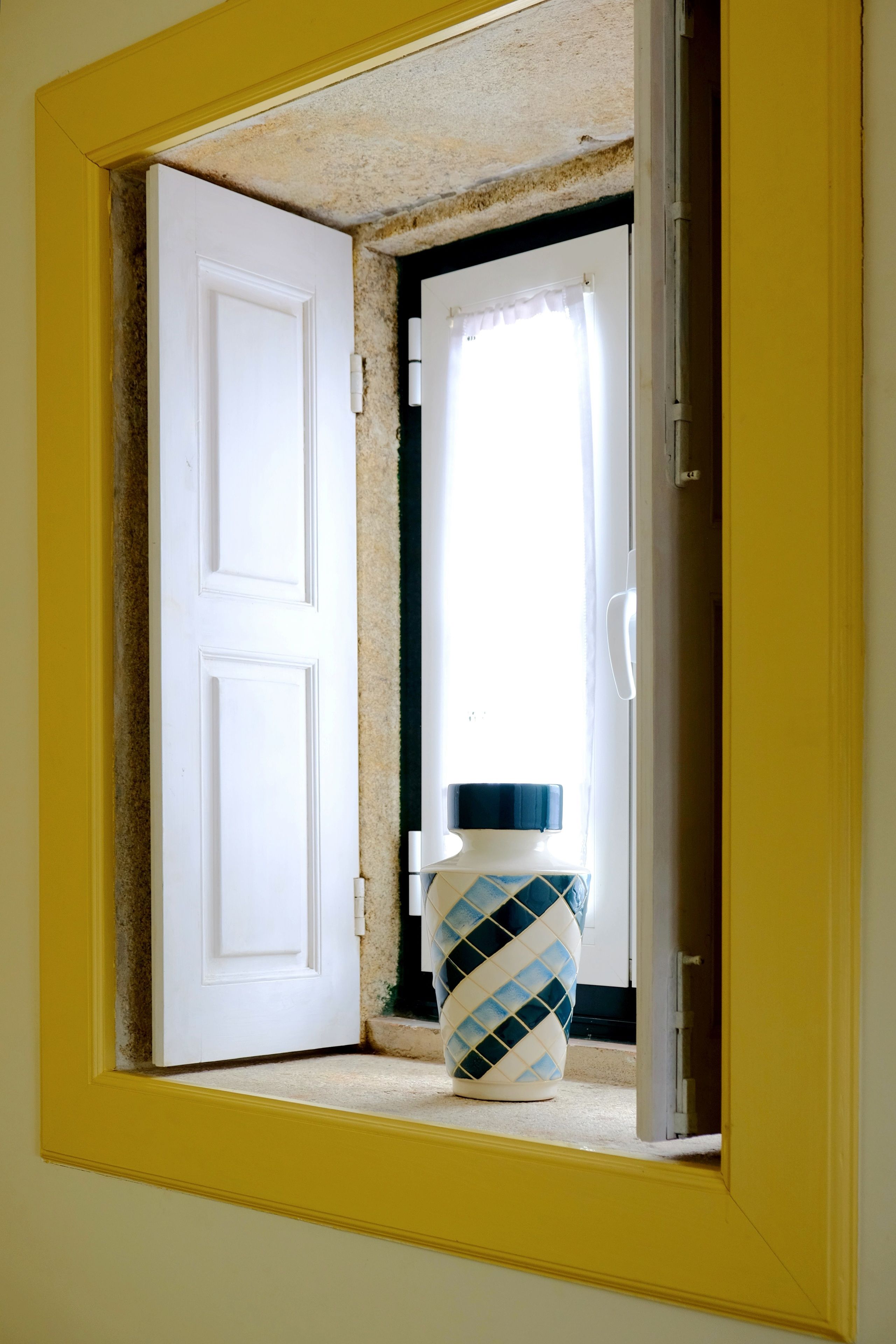 A doorway with a white door, a window with white curtains, and a patterned vase on the floor.