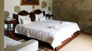 A bedroom with a large bed, stone walls, wooden beams, and a stone fireplace. - Casa Mindela Farmhouse (Vila do Conde)