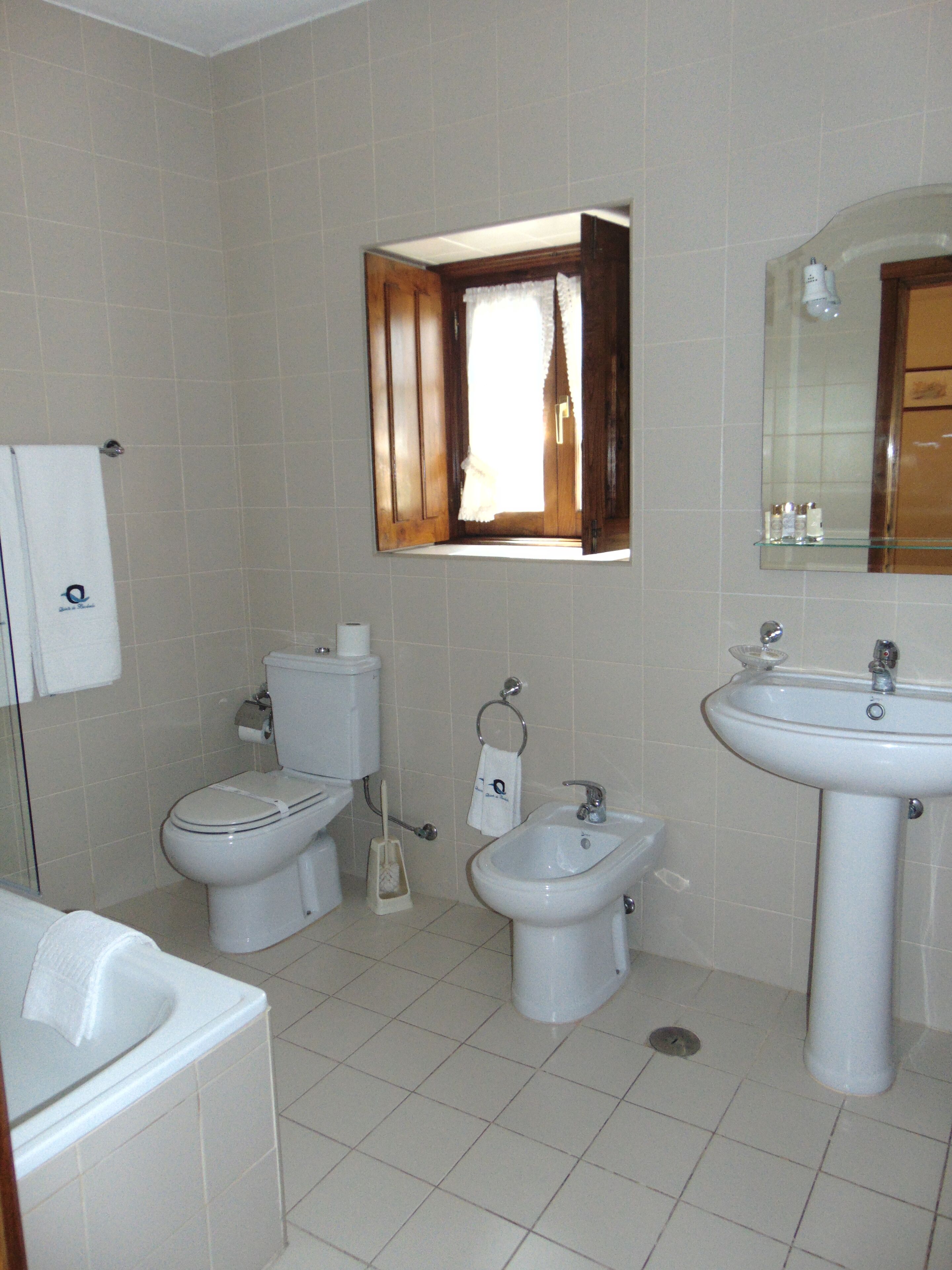 Een badkamer met toilet, bidet, wastafel en een spiegel boven de wastafel.