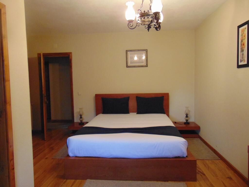 Un dormitorio con una cama de madera, dos mesitas de noche, una lámpara de araña y un cuadro en la pared.