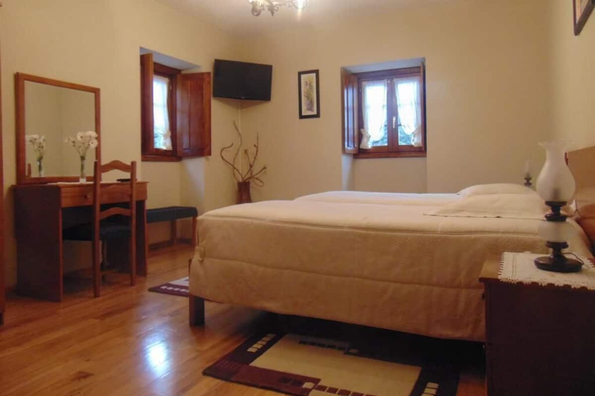 Ein Schlafzimmer mit Bett, Schreibtisch, Stuhl, Spiegel, Fernseher und Fenster.