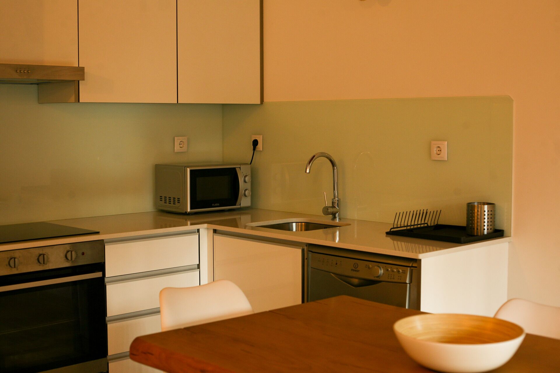 A compact kitchen with a microwave, sink, dishwasher, and a wooden table with a bowl.