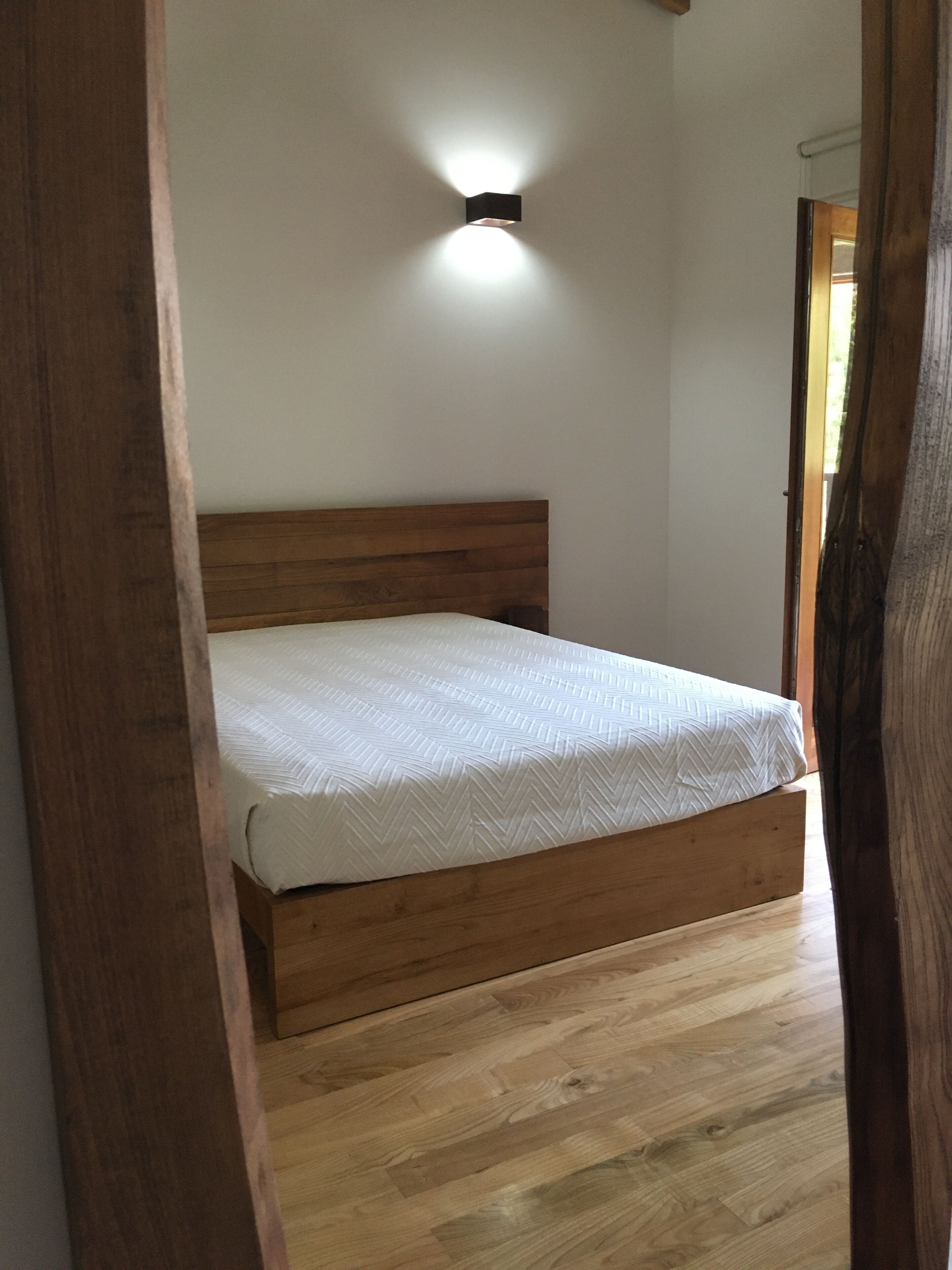 A bedroom with a wooden bed frame, a white mattress, and a wall-mounted light fixture.